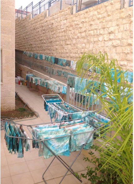 Hands dipping white tzitzit into vibrant buckets of colorful dye